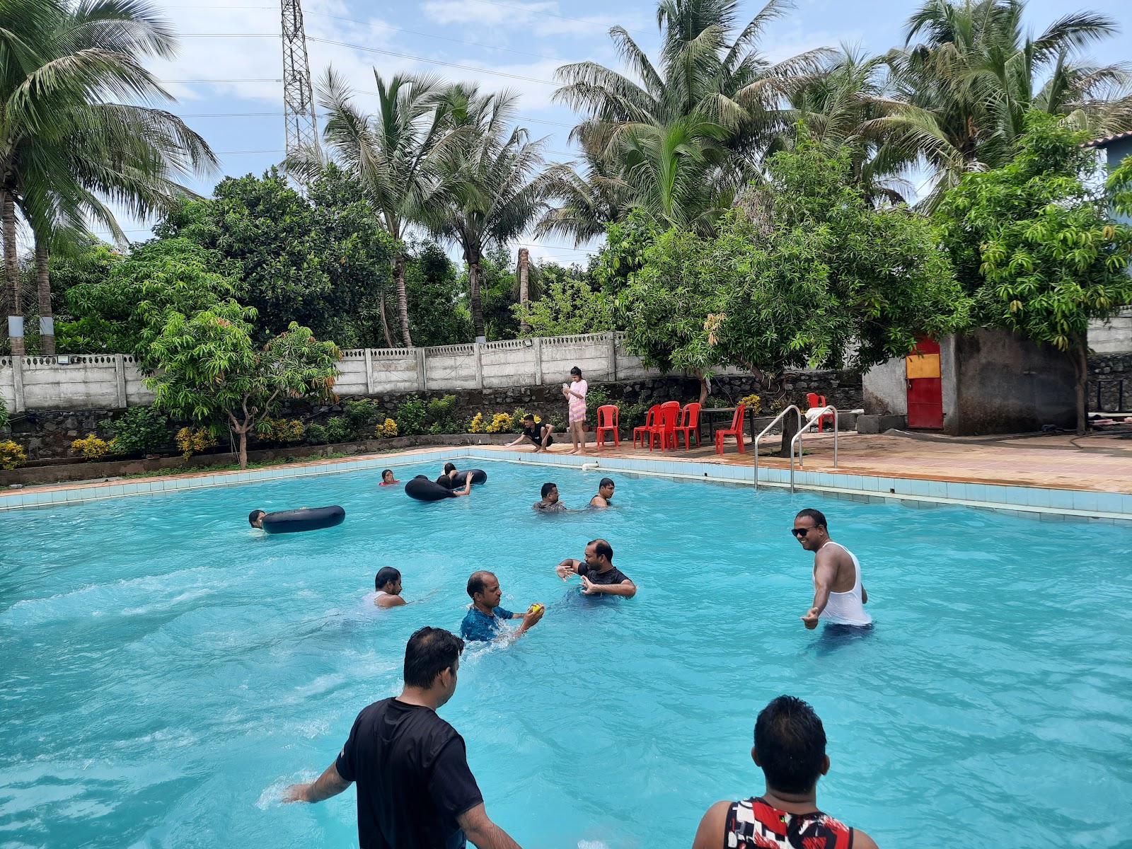 Guests enjoying the pool surrounded by palm trees at Kanchan Farmhouse